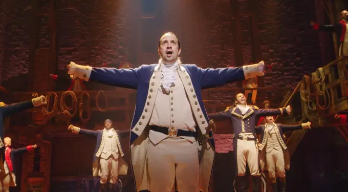 Lin-Manuel Miranda performs on stage with outstretched arms in Hamilton