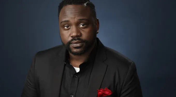 Brian Tyree Henry in black suit with red pocket square against dark background