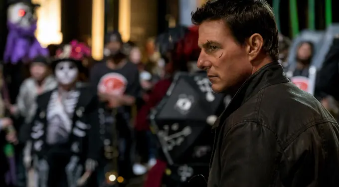Tom Cruise with facial scars in jacket at nighttime parade with skeleton costumes