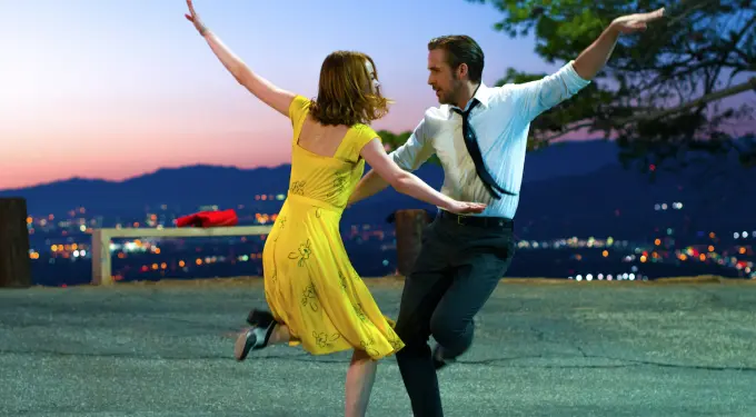 Man and woman dancing outdoors at dusk with city skyline behind