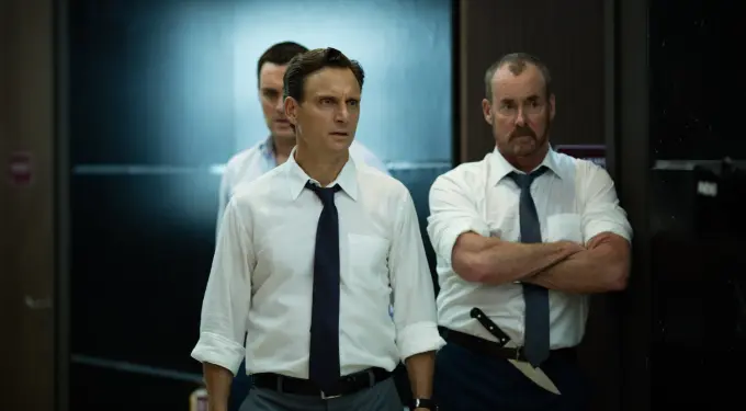 Three men in white shirts and ties stand tensely in hallway, one with knife