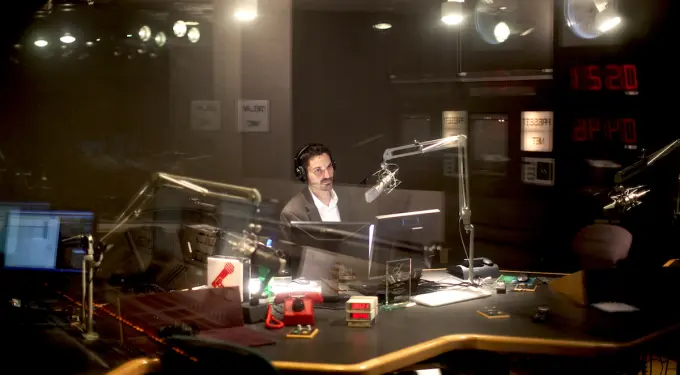 Man in suit hosting podcast in radio studio wearing headphones