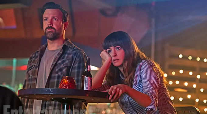 man and woman sit at table in dim bar with drinks