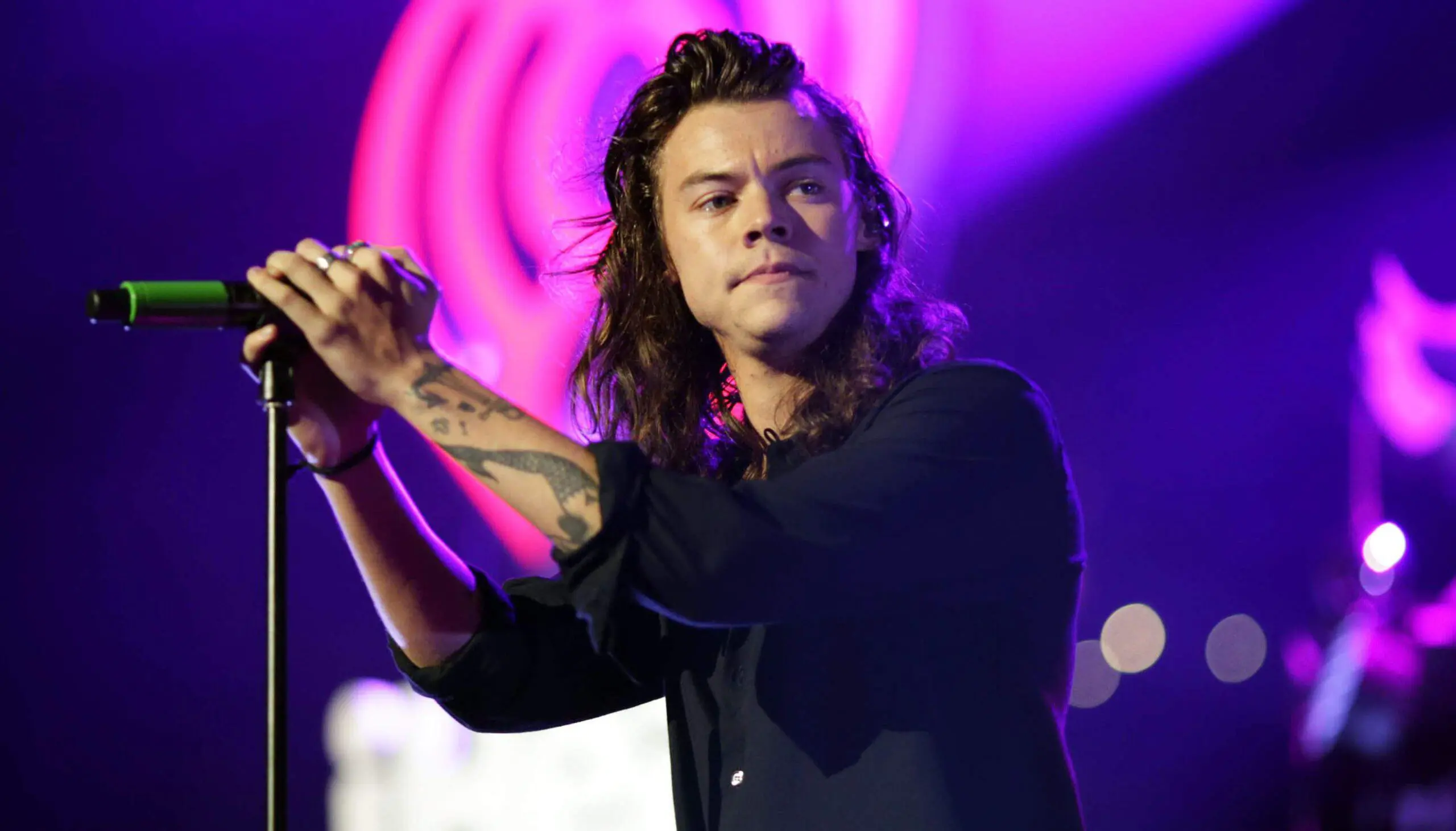 Harry Styles singing on stage with microphone stand and purple lights