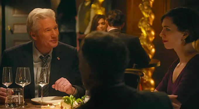 Richard Gere in suit talks across table at restaurant dinner scene