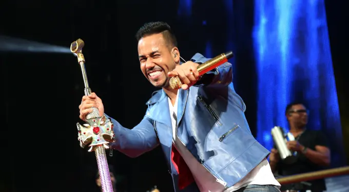 Romeo Santos singing and holding decorated mic stand on stage