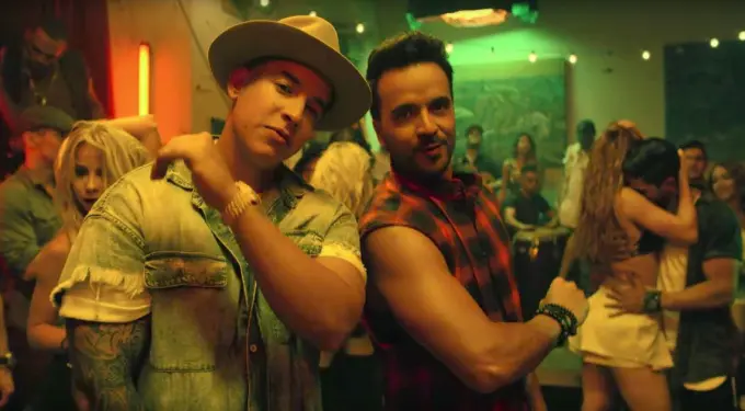 Two men posing at a crowded club, one in hat and denim, other in sleeveless shirt