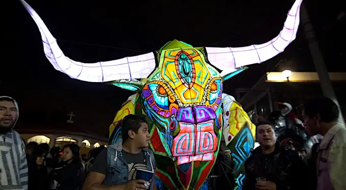 people around large colorful illuminated bull sculpture at night