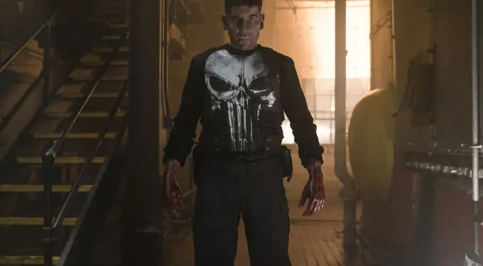The Punisher stands bloodied in tactical gear in dark industrial hallway
