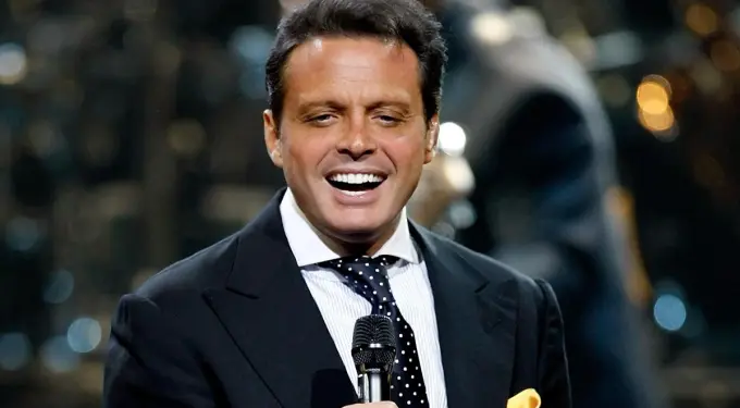 Luis Miguel in suit singing on stage holding microphone