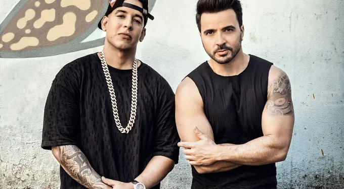 Daddy Yankee and Luis Fonsi stand side by side in black shirts with tattoos visible