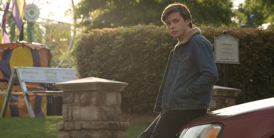 Nick Robinson leans on car near carnival rides in Love Simon scene