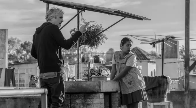 Scene from Alfonso Cuaron’s ROMA showing two characters by an outdoor sink
Man gestures while young woman leans on brick outdoor sink
