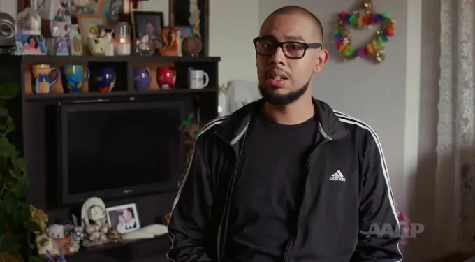 Man with beard and glasses speaking in casual Adidas jacket indoors