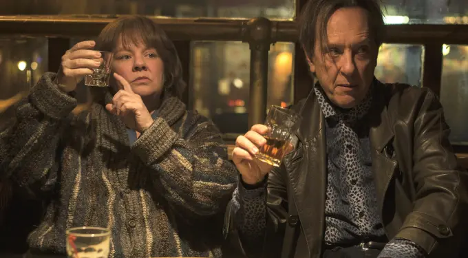 Melissa McCarthy and Richard E. Grant hold drinks in a bar scene