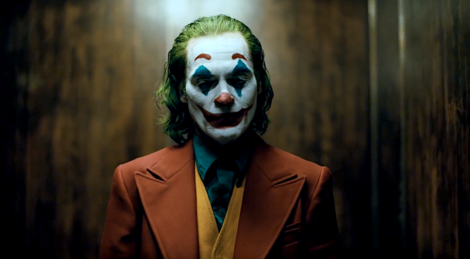 Joker character in clown makeup wearing orange suit and yellow vest