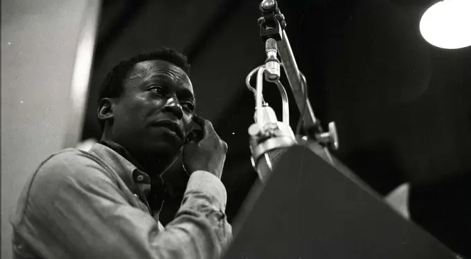 Miles Davis in a recording or live performance setting, spotlighted at microphone.
Miles Davis at microphone during recording or performance