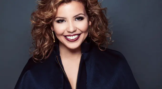Justina Machado in a professional headshot with curly hair and gold earrings
Justina Machado close-up portrait smiling at camera in navy jacket