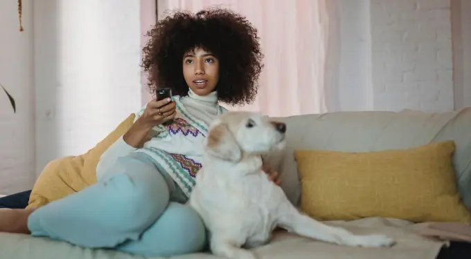 Woman reclining on couch holding remote with dog beside her