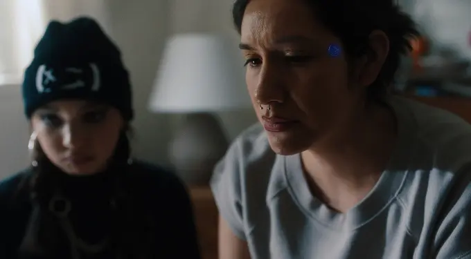 Two women indoors, one with facial piercings looks pensive