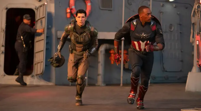 Danny Ramirez and Anthony Mackie running in superhero costumes on a ship